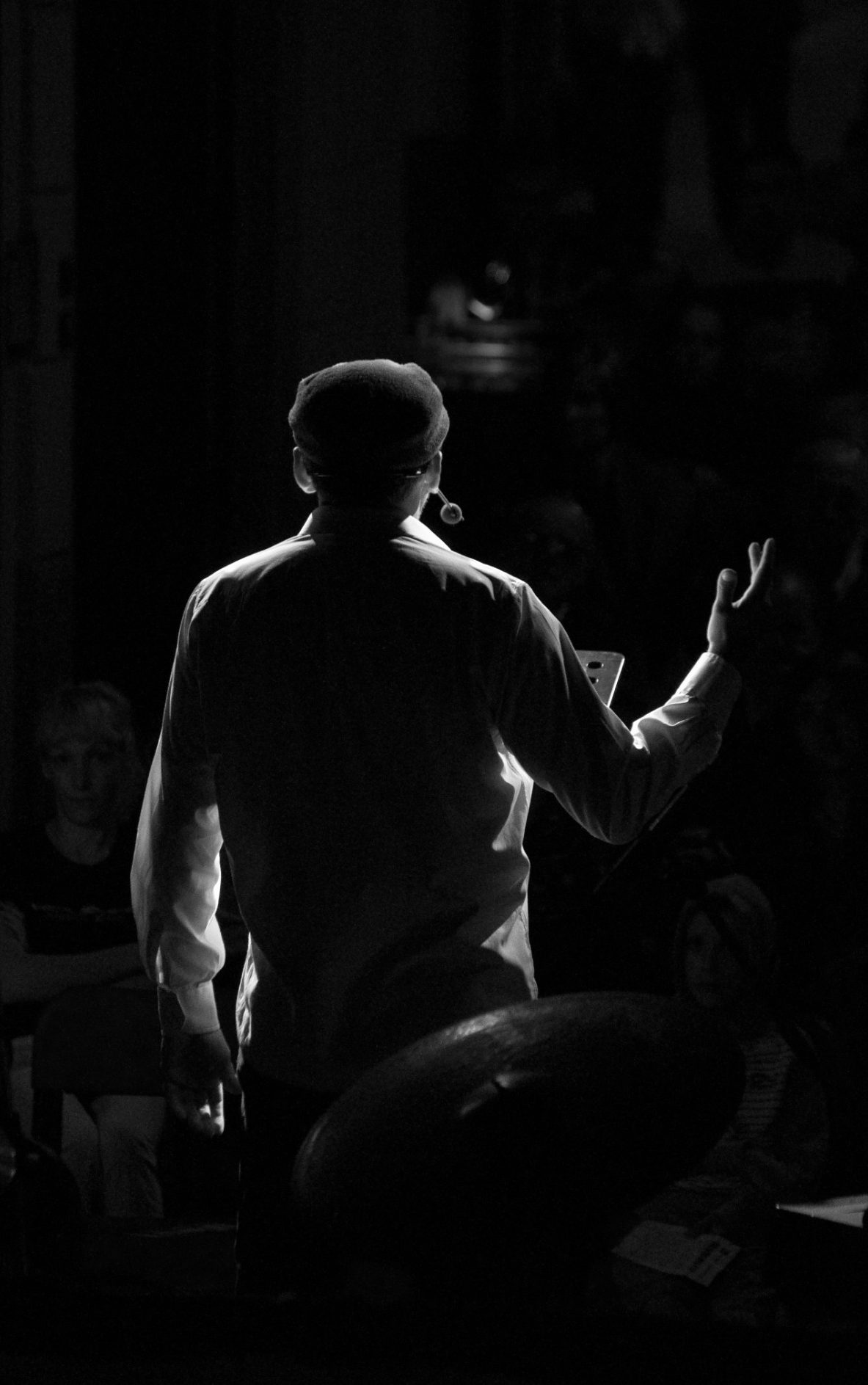Hombre de espaldas gesticulando durante una presentación en un ambiente oscuro.