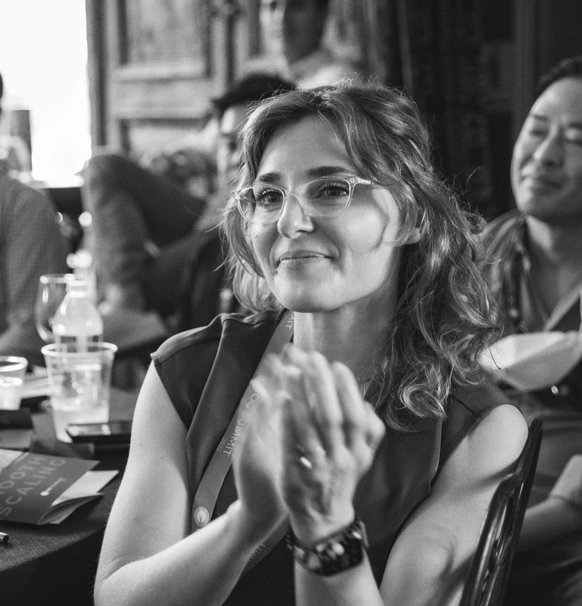 Mujer con gafas sonriente, aplaudiendo en un ambiente informal y acogedor.