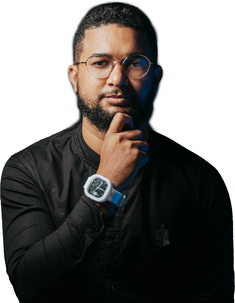 Hombre con barba, gafas y reloj, posando con una mano en el mentón. Lleva una camisa negra.