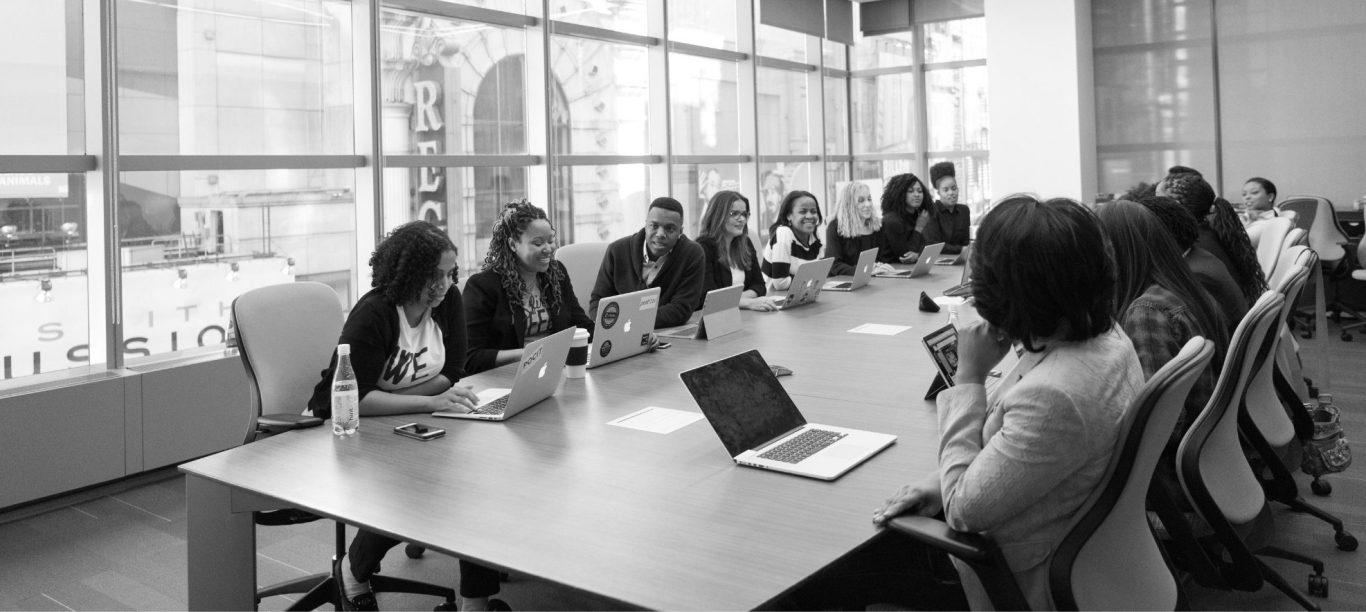 Reunión en una mesa larga con varias personas conversando y usando computadoras portátiles.
