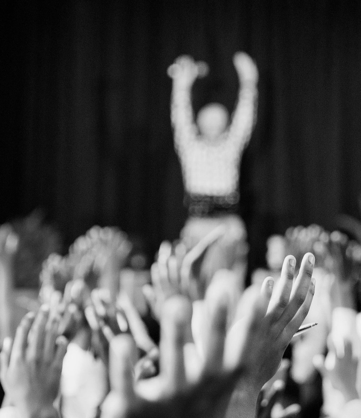 Multitud de manos levantadas en apoyo, con una figura al fondo en un escenario.